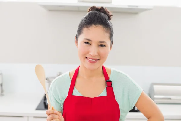 Lachende vrouw in rode schort met een houten lepel in keuken — Stockfoto