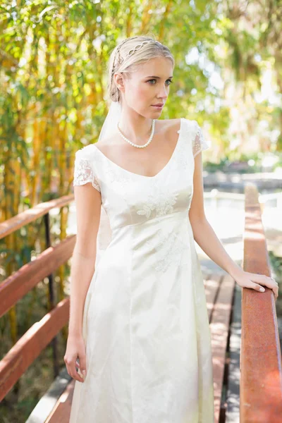 Content blonde bride in pearl necklace standing on a bridge — Stock Photo, Image