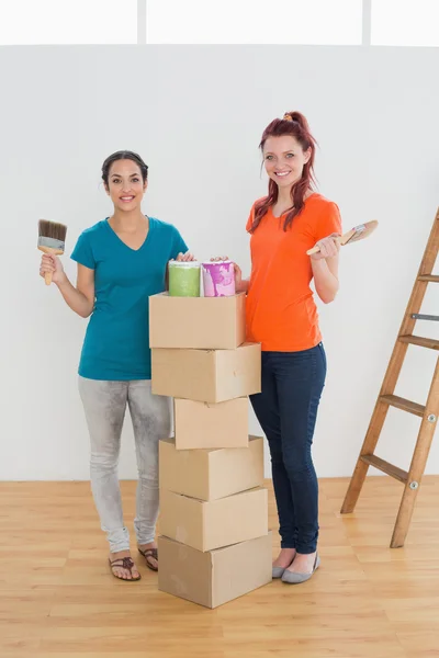 Vrienden met verf penselen, blikjes en vakken in nieuwe huis — Stockfoto