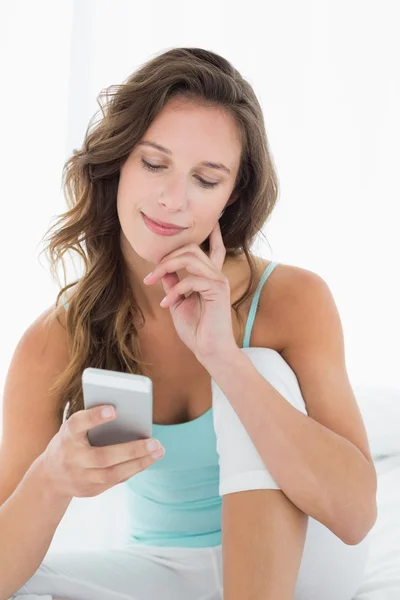 Mujer sonriente mirando el teléfono móvil en la cama —  Fotos de Stock