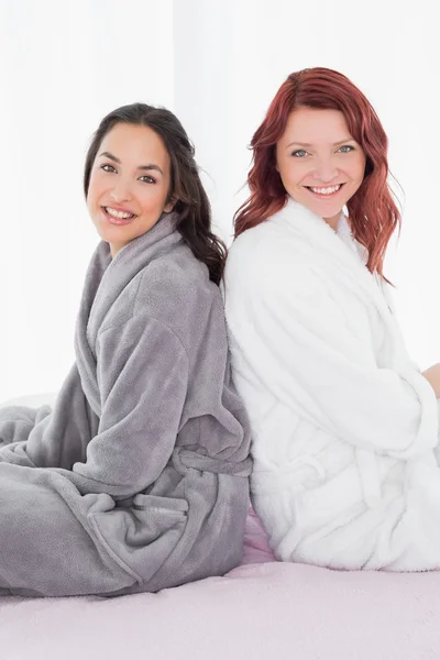 Freundinnen in Bademänteln sitzen Rücken an Rücken auf dem Bett — Stockfoto