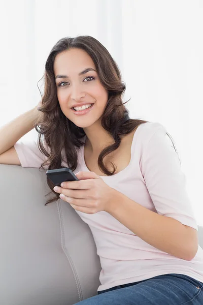 Sorridente messaggio di testo giovane donna sul divano a casa — Foto Stock