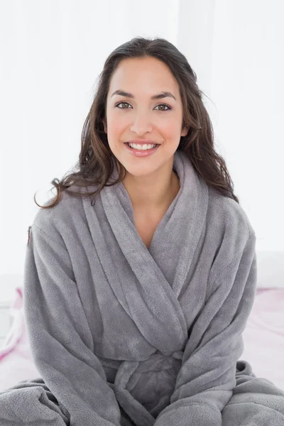Portret van een jonge vrouw in badjas zittend op bed — Stockfoto