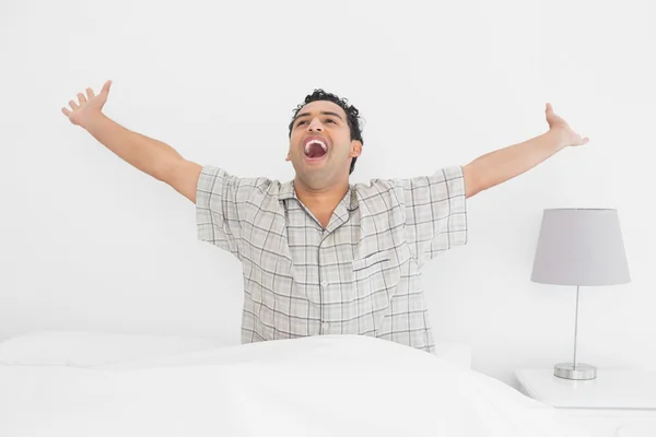 Sorridente giovane uomo allungando le braccia a letto — Foto Stock
