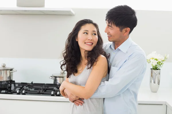 Smiling man embracing woman from behind in kitchen — Stock Photo, Image