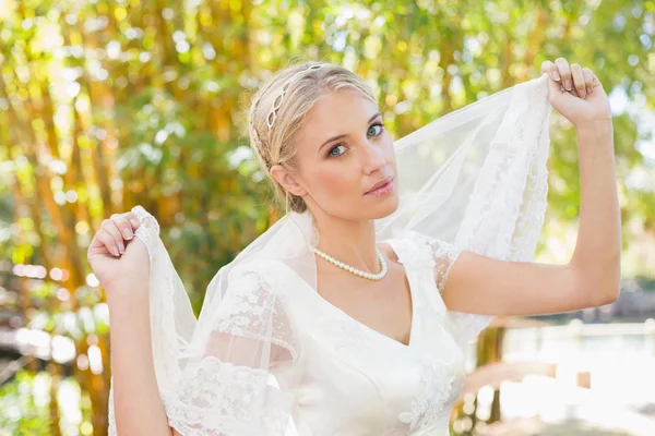 Pretty content blonde bride holding her veil out smiling at camera — Stock Photo, Image