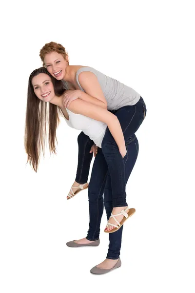 Full length portrait of a young female piggybacking friend — Stock Photo, Image