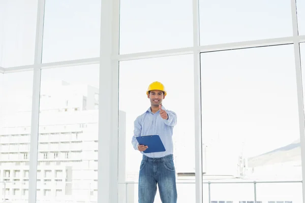 Arquiteto em chapéu duro com prancheta gesticulando polegares no escritório — Fotografia de Stock