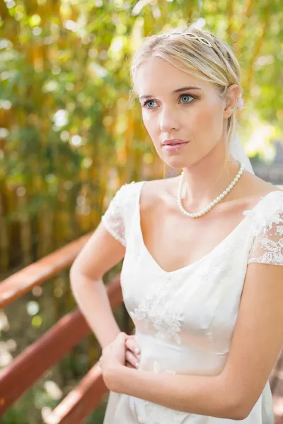 Bella sposa bionda in piedi su un ponte guardando altrove — Foto Stock