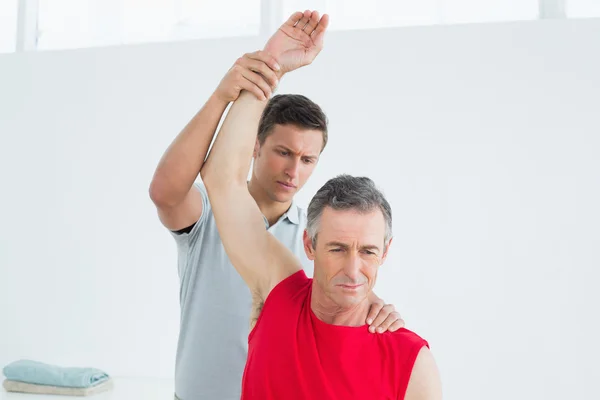 Fisioterapeuta masculino estirando un brazo de hombre maduro — Foto de Stock