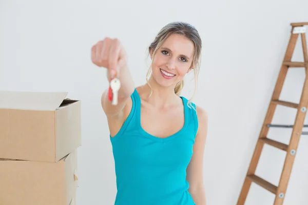 Woman holding out with key besides boxes in new house — Stock Photo, Image