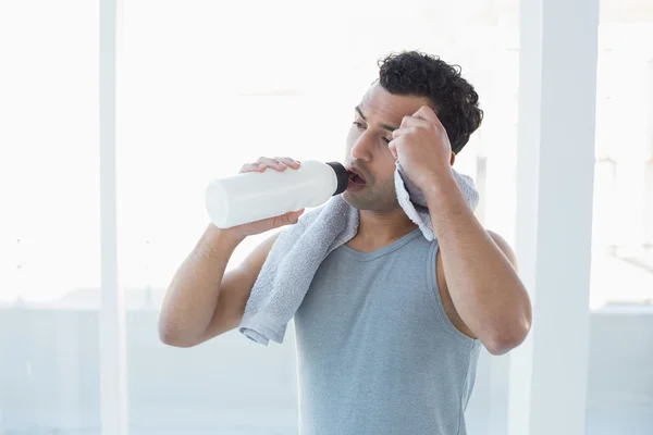 Homem bebendo água enquanto limpa o suor com toalha no estúdio de fitness — Fotografia de Stock