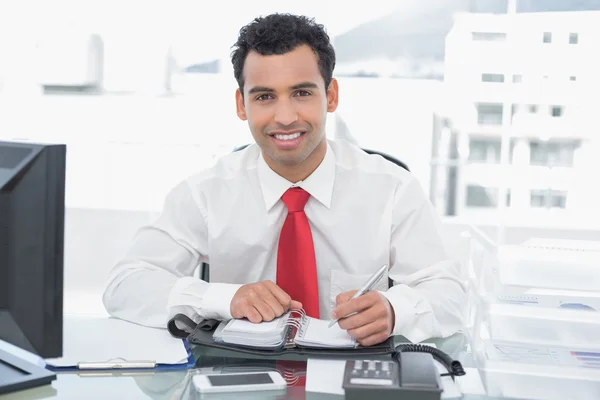 Усміхнений молодий бізнесмен пише в щоденнику в офісі — стокове фото