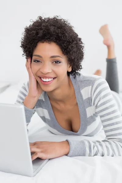 Sorridente giovane donna utilizzando il computer portatile a letto — Foto Stock