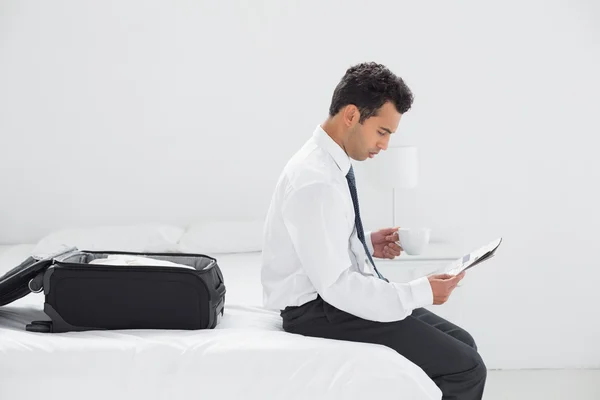 Podnikatel s cup, čtení novin v hotelovém pokoji — Stock fotografie