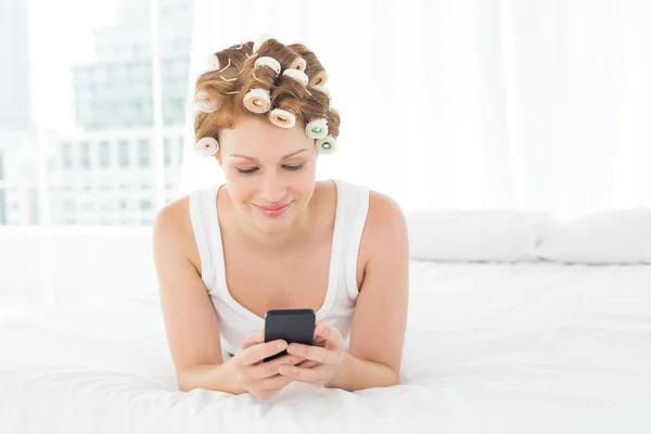 Kobieta w włosów lokówki tekst wiadomości podczas leżenia w łóżku — Zdjęcie stockowe