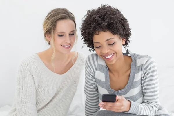 Sonrientes amigas leyendo mensajes de texto en la cama —  Fotos de Stock