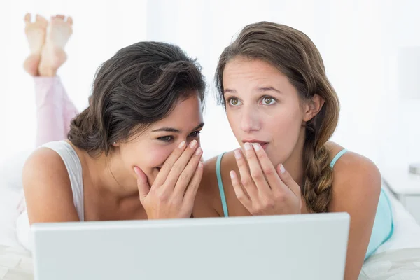 Relaxed female friends with laptop gossiping in bed — Stock Photo, Image
