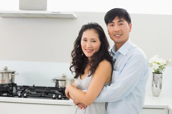 Jonge man omhelst vrouw van achter in de keuken — Stockfoto