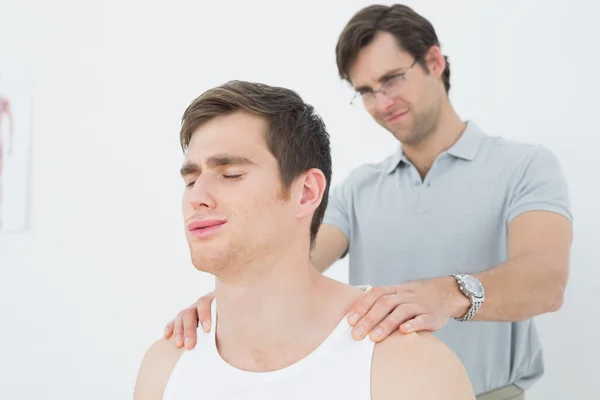 Fisioterapeuta masculino masajeando un hombro de hombre joven — Foto de Stock