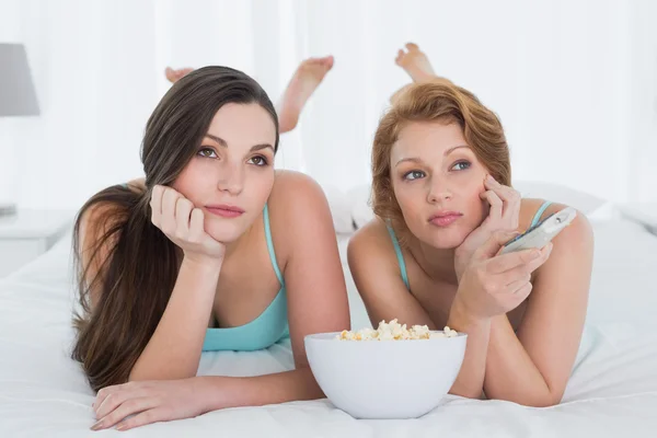 Vrouwelijke vrienden met afstandsbediening en popcorn in bed — Stockfoto