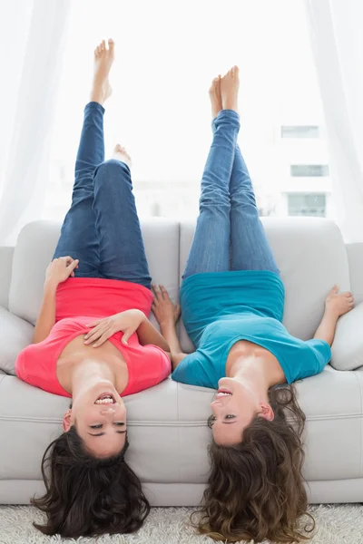 Улыбающиеся друзья, лежащие на диване с ногами в воздухе дома — стоковое фото