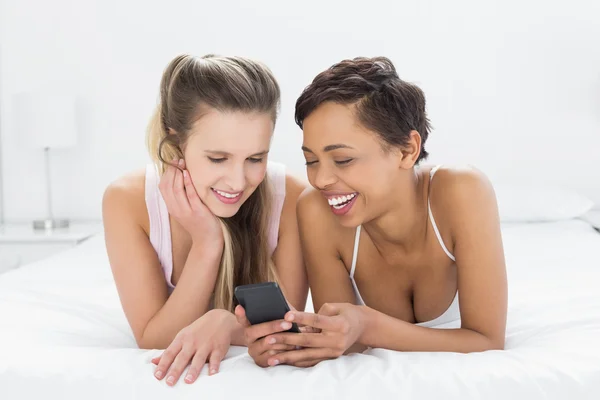 Sorrindo amigas lendo mensagem de texto na cama — Fotografia de Stock