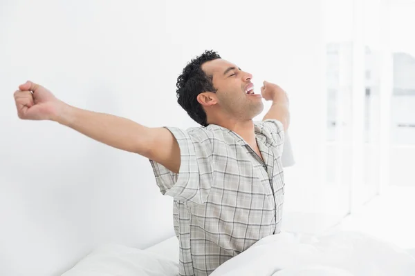 Joven estirando los brazos en la cama — Foto de Stock