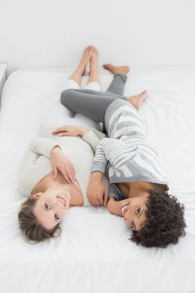 Dos alegres amigas jóvenes tumbadas en la cama —  Fotos de Stock