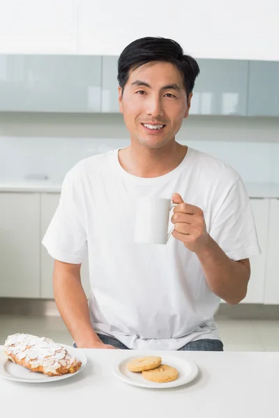 Smiling young man drinking coffee in kitchen — Stock Photo, Image