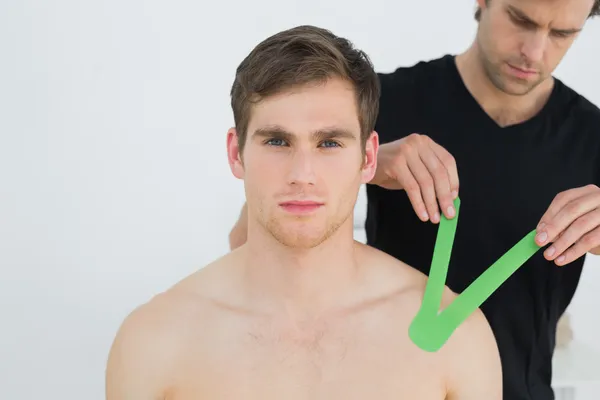 Physiotherapist putting on kinesio tape on patients shoulder — Stock Photo, Image