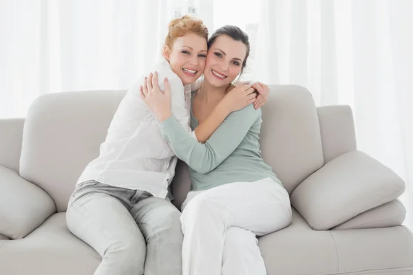 Vrolijke jonge vrouwelijke vrienden omarmen in woonkamer — Stockfoto