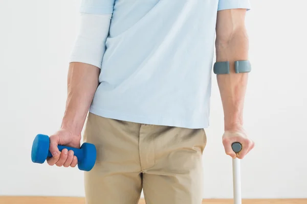 Mid section of a young man with crutch and dumbbell — Stock Photo, Image