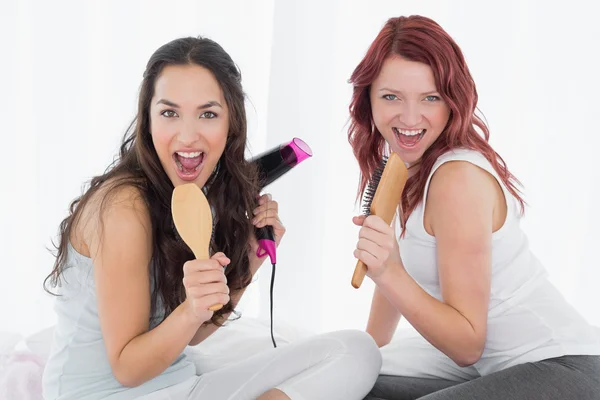 Cheerful young female friends singing into hairbrushes — Stock Photo, Image