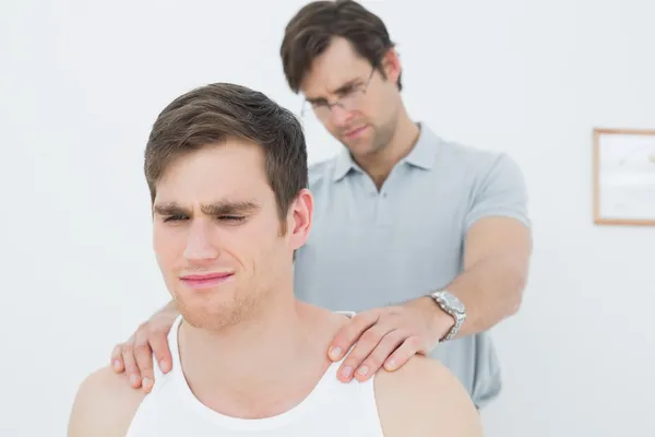 Fisioterapeuta masculino masajeando un hombro de hombre joven — Foto de Stock