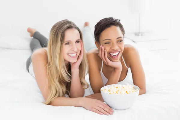 Allegro amici femminili con ciotola popcorn sdraiato a letto — Foto Stock