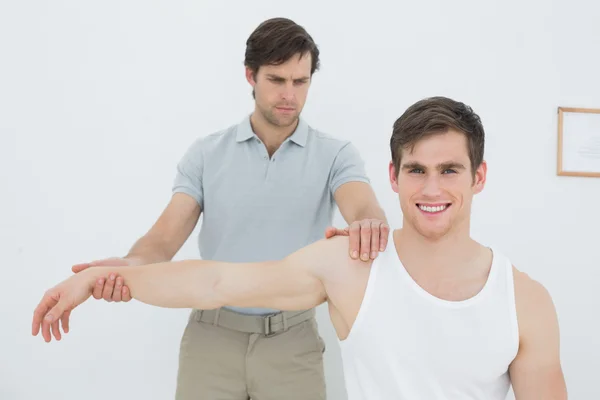 Fisioterapeuta masculino examinando un brazo de hombre joven — Foto de Stock