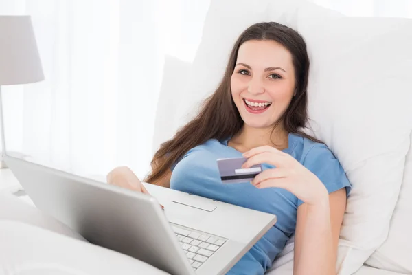 Cheerful casual woman doing online shopping in bed — Stockfoto