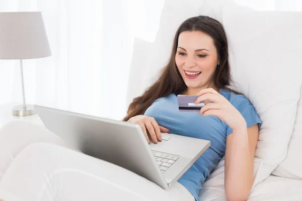 Glada casual kvinna gör online shopping i sängen — Stockfoto