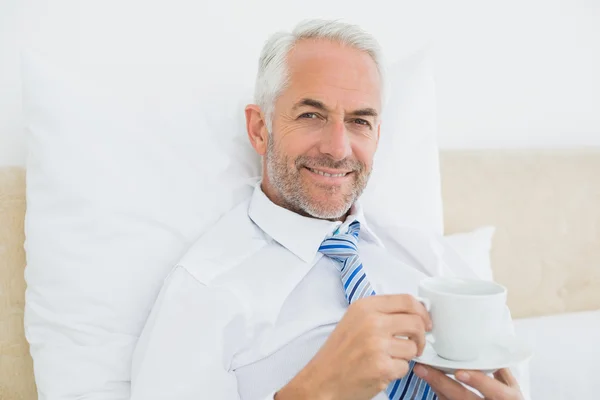 Lächelnder Geschäftsmann mit einer Tasse Tee im Bett — Stockfoto