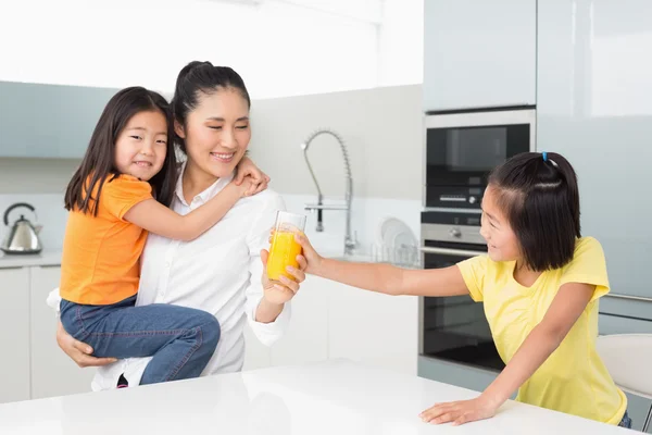 Dziewczyna oferuje jej matka szklankę soku pomarańczowego w kuchni — Zdjęcie stockowe