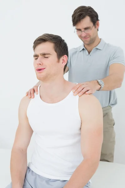 Fisioterapeuta masculino masajeando un hombro de hombre joven —  Fotos de Stock
