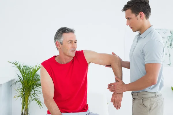 Sjukgymnast undersöka en leende mogen mans arm — Stockfoto