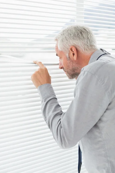 Rear view of a businessman peeking through blinds — Stock Photo, Image