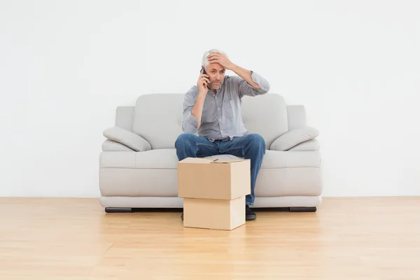 Hombre molesto usando cellpone en sofá con cajas en casa — Foto de Stock