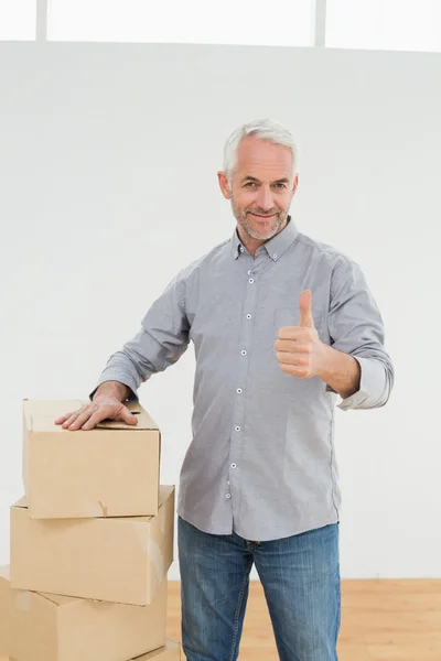 Smiling man with boxes gesturing thumbs up in a new house — Stock Photo, Image