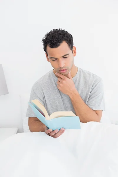 Serious relaxed man reading book in bed — Stock Photo, Image