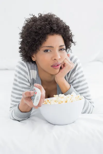 Žena s dálkovým ovládáním a mísa popcornu ležící v posteli — Stock fotografie