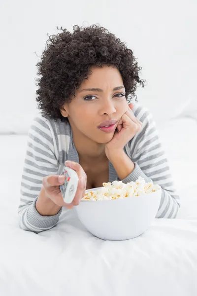 Mujer con control remoto y palomitas de maíz en la cama — Foto de Stock