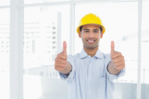 Handyman en amarillo duro sombrero gesto pulgares hacia arriba en la oficina —  Fotos de Stock